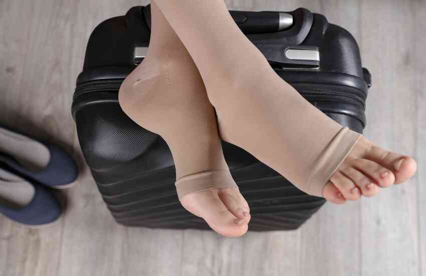 Ženské nohy v kompresních punčochách položené na kufru.