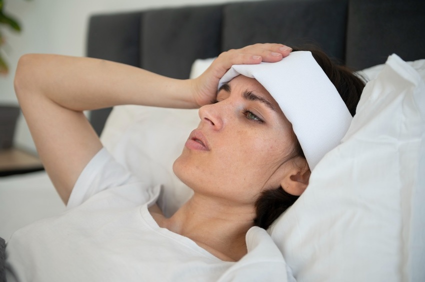 Žen si dává chladivý obklad proti bolesti hlavy.
